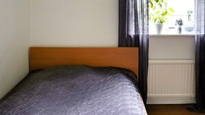 Un dormitorio con cama, ventana con cortinas y un radiador.