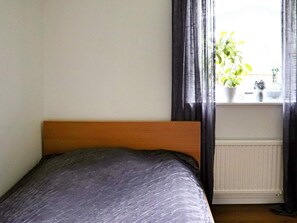 Ein Schlafzimmer mit einem Bett, einem Fenster mit Vorhängen und einer Heizung.