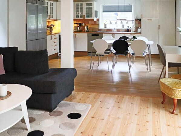 A modern kitchen with white cabinets, a dining area with a table and chairs, and a living room with a sofa and a coffee table. - 4 Star Holiday Home in Mellbystrand (Mellbystrand)