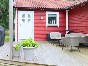 Une maison rouge avec une porte blanche, une fenêtre dotée d’un cadre blanc et un petit balcon agrémenté de meubles en osier et de plantes en pot.