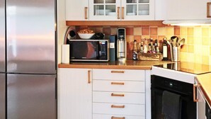 Una cocina con armarios blancos, microondas, cafetera y escurreplatos.