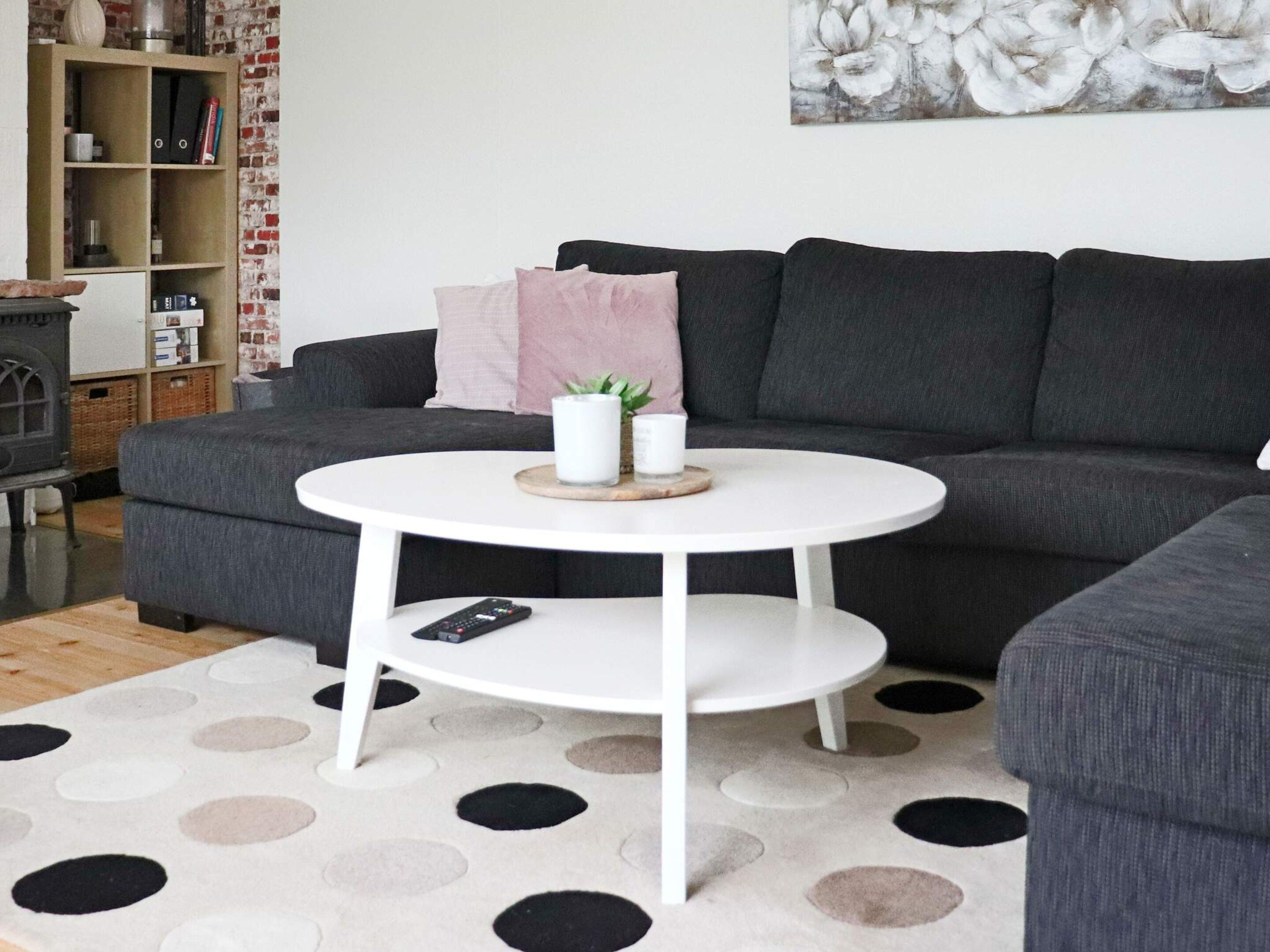 Un salon avec un canapé gris, une table basse blanche et un tapis à pois.