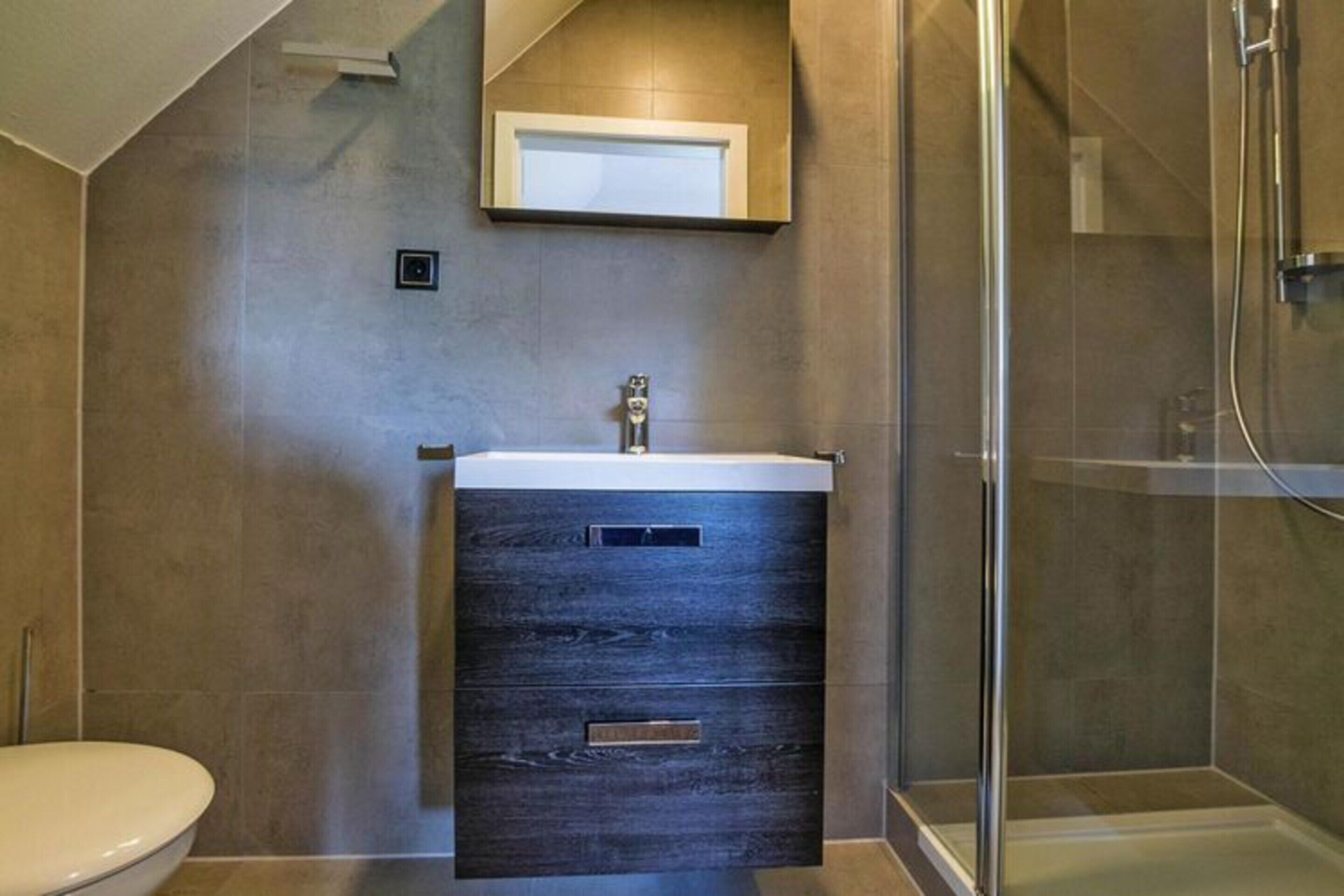 Ein modernes Badezimmer mit einer Duschkabine aus Glas, einem integrierten Waschbecken mit dunklen Holzschrank und einem kleinen Fenster über dem Waschbecken.