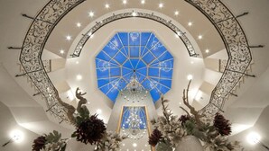 A grand hall with a large blue stained glass window, a central chandelier, and ornate metal railings. - Ferienhaus im Van der Valk Resort in Linstow (Dobbin-Linstow)