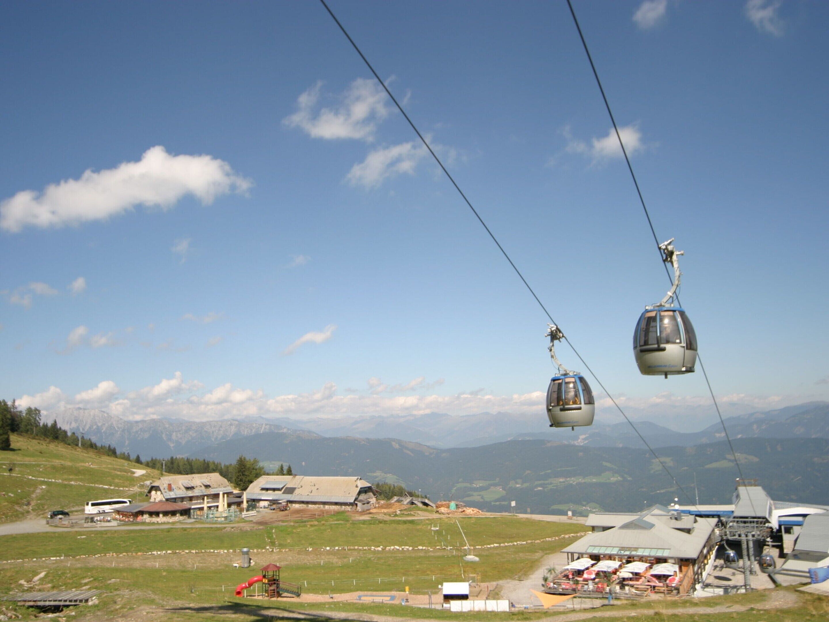 A cable car system in a mountainous area with buildings and a parking lot in the foreground.