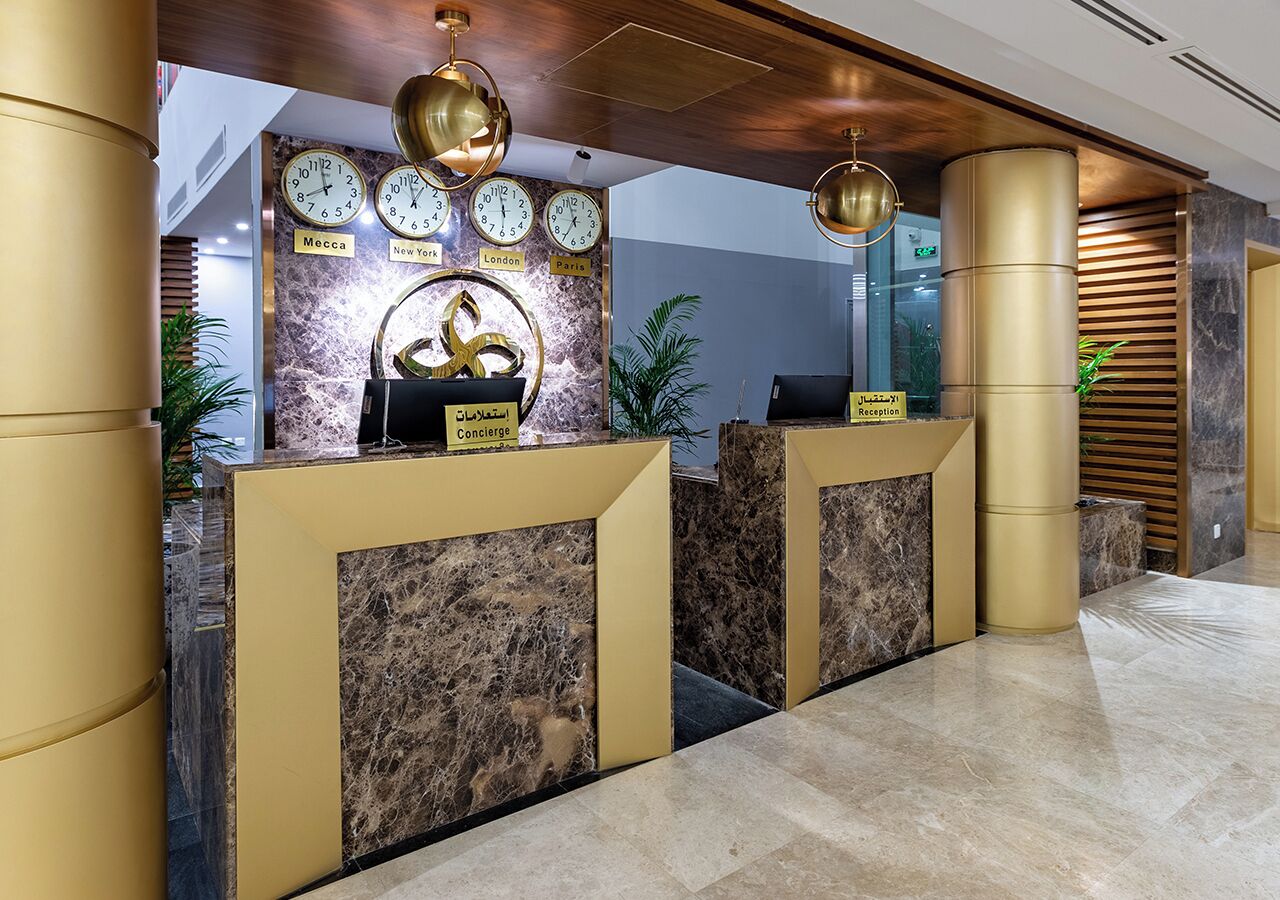 Un área de recepción con mostradores de mármol, relojes mostrando diferentes husos horarios y un mostrador de recepción identificado como "Concierge".