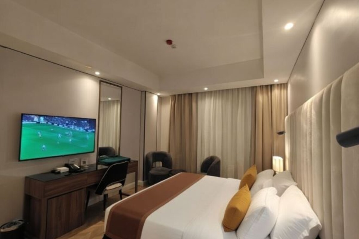 Une chambre d’hôtel équipée d’un lit, d’un bureau, d’une chaise, d’une télévision et de rideaux.