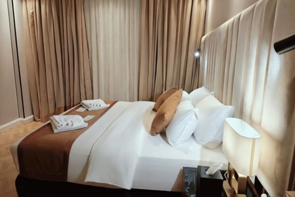 Une chambre d’hôtel avec un lit, des oreillers, une table de chevet avec une lampe et un rideau en arrière-plan.