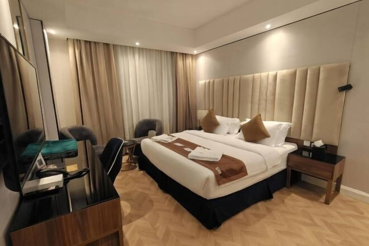 Egy modern szállodaszoba, amelyben egy nagy ágy, egy íróasztal székkkel, egy kis asztal és egy tükör található.