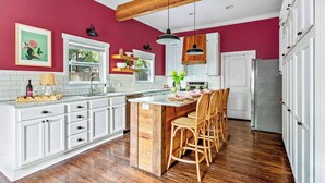 A kitchen with white cabinets, a wooden island, and a red accent wall. - The Pepper Place (Waco)