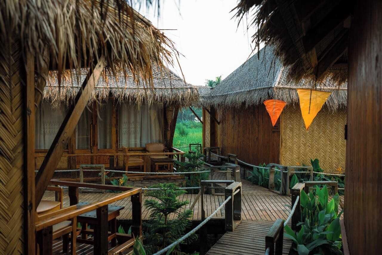 A wooden deck with thatched-roof huts, wooden furniture, and rope barriers.