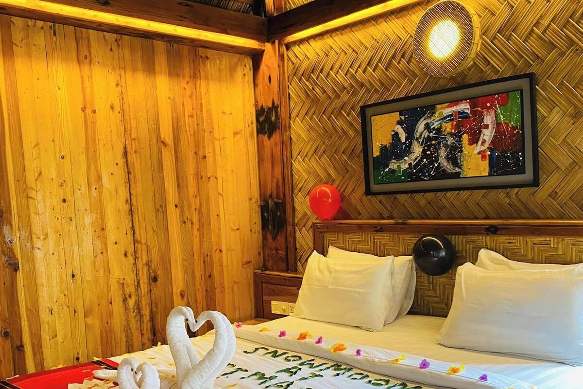 Habitación de hotel con decoración de madera, cama con ropa blanca, una colcha roja y negra, y un cuadro en la pared.