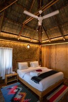 Quarto de madeira com uma cama, um criado-mudo, um telefone, um ventilador de teto e parede com padrão herringbone.