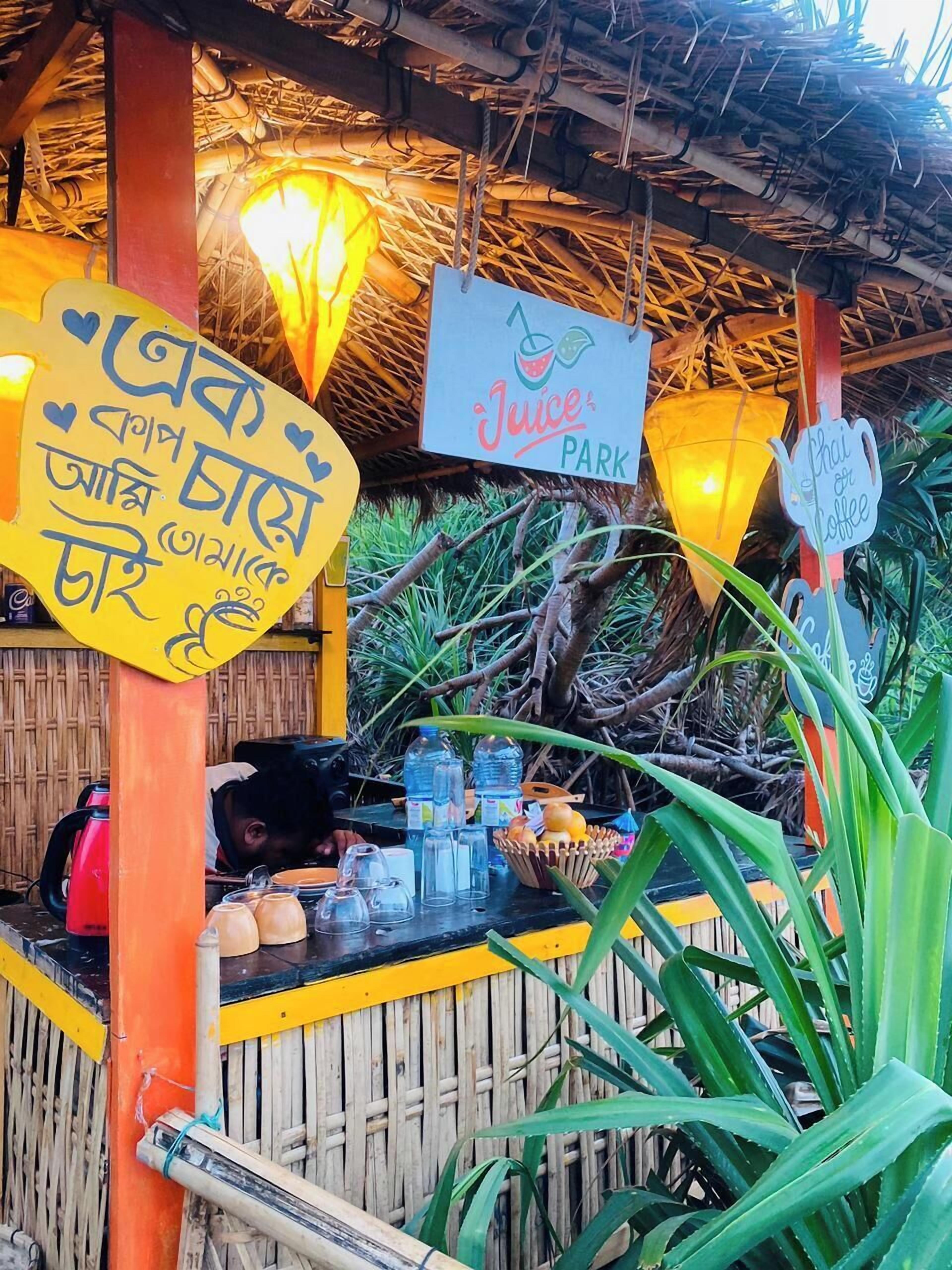 A rustic outdoor juice bar with a thatched roof, bamboo walls, and a sign indicating it is a juice park.
