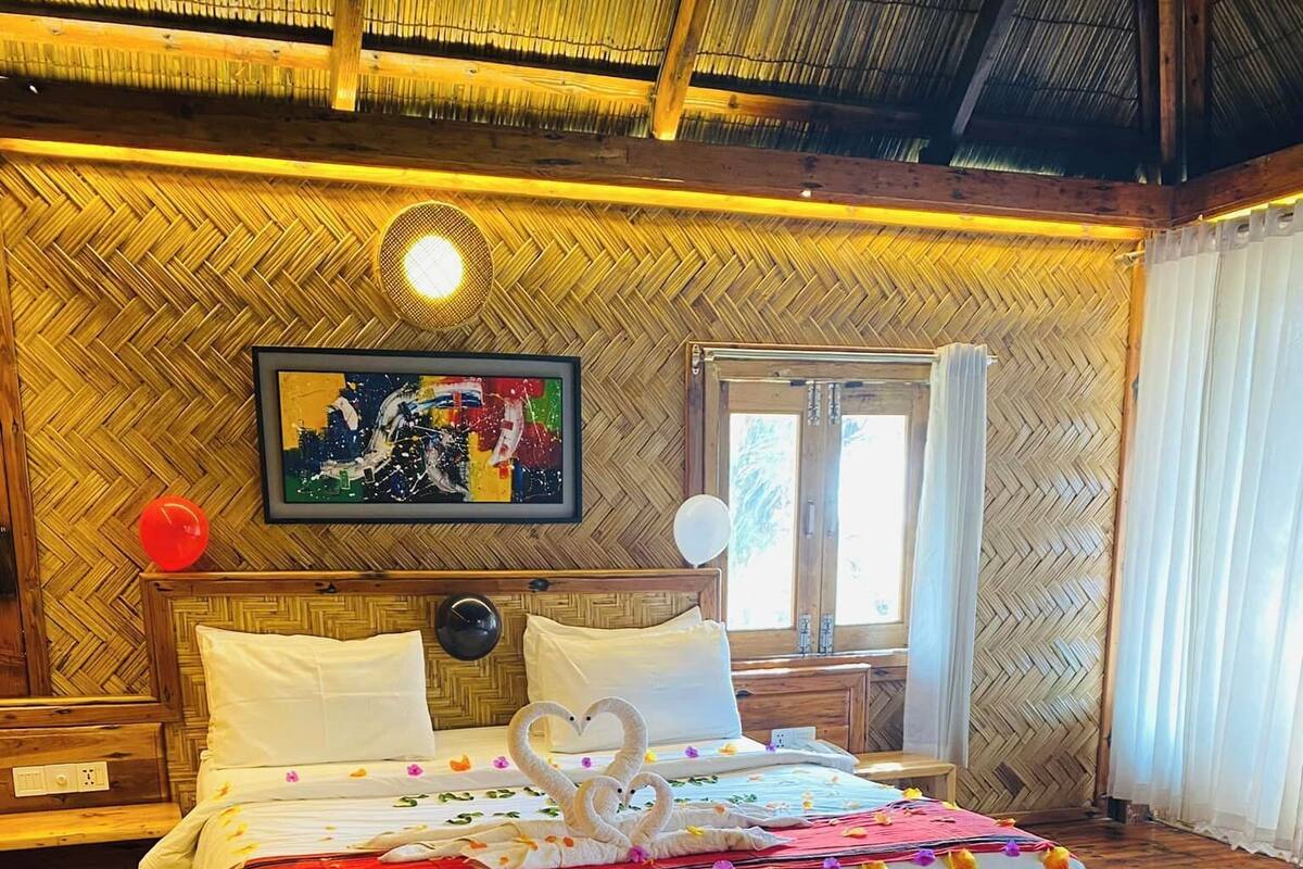 Habitación de hotel con una pared de madera con patrón de espiga, una cama con ropa blanca y una decoración con forma de corazón, y una alfombra colorida en el suelo.