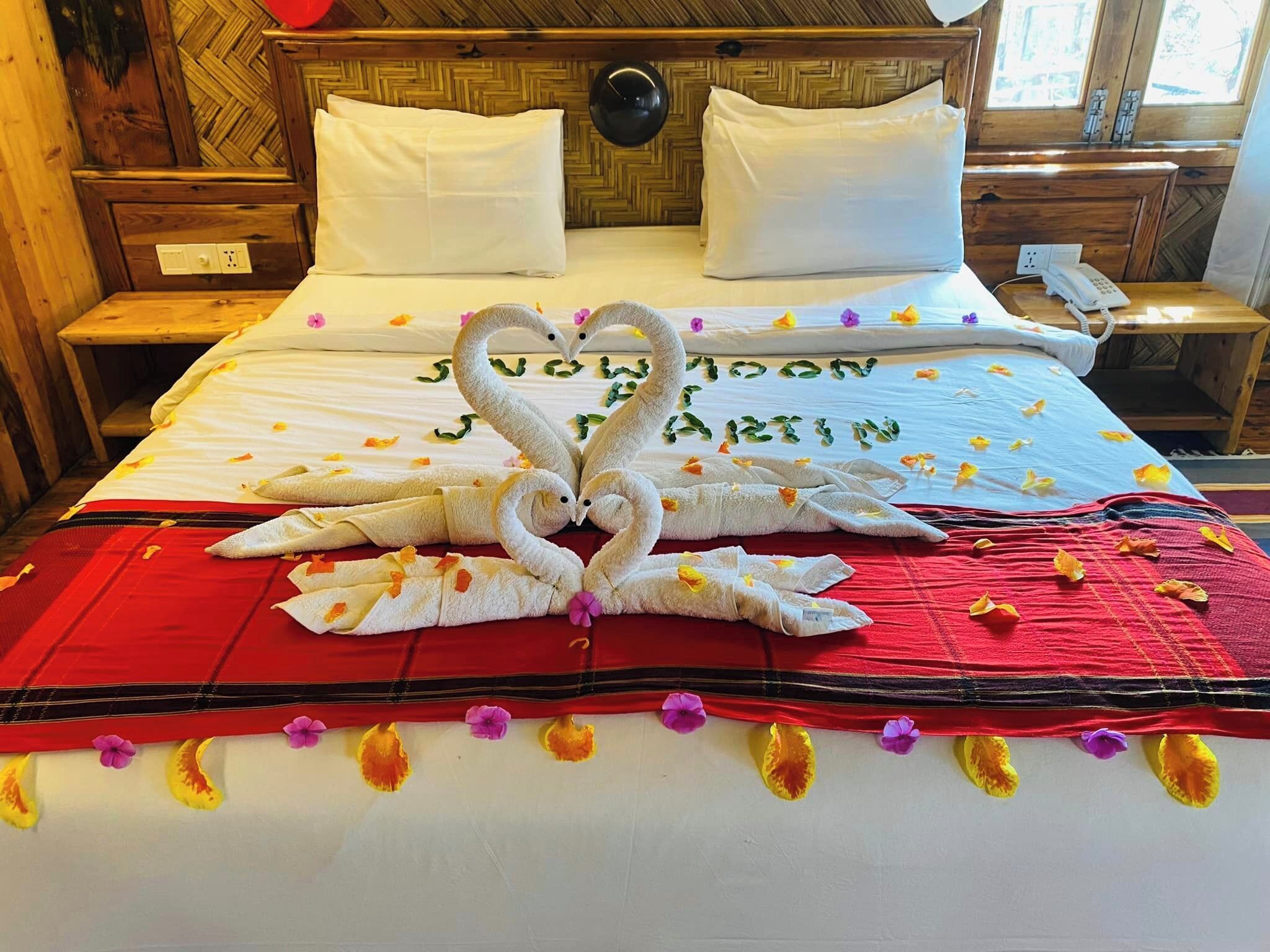 Un lit avec une couvre-lit rouge, des oreillers blancs et une disposition de serviettes en forme de cœur sur le lit.