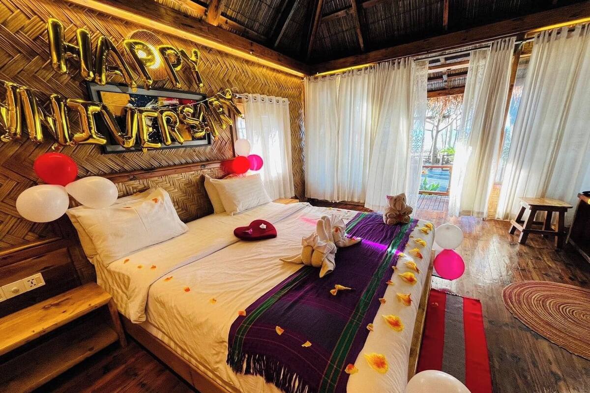 Una habitación con una cama, un cartel que dice 'Feliz aniversario', globos y un gato.