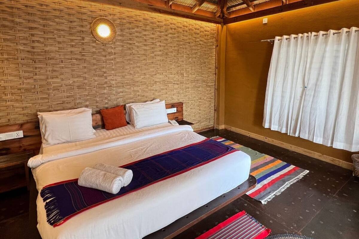 Una cama con ropa blanca, un tapete a rayas de colores y un panel de pared tejido.