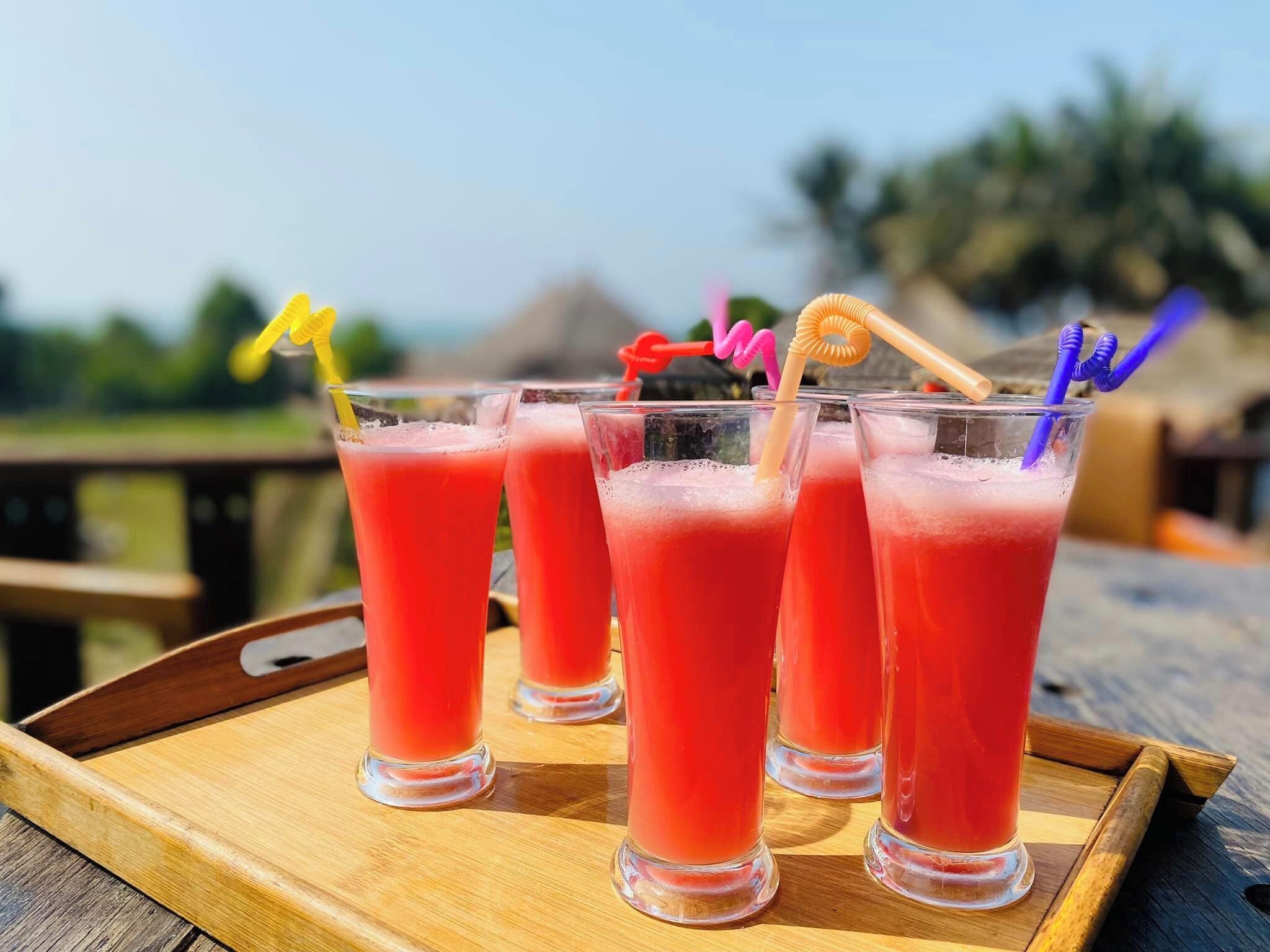 Four glasses of red beverage on a wooden tray.