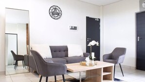 Ett modernt vardagsrum med en grå soffa, två fåtöljer, ett soffbord i trä och en dekorativ väggklocka.