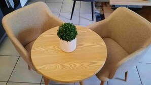 Ett runt träbord med en krukväxt i mitten, omgivet av två beige stolar.