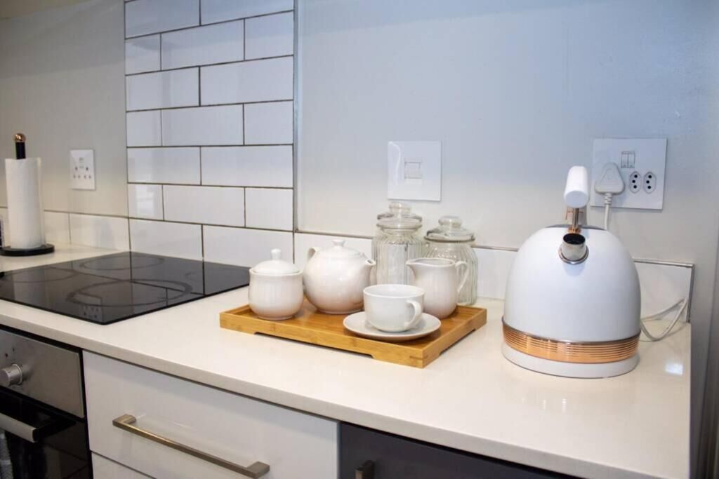 Une cuisine dotée d’une plaque de cuisson à induction noire, de meubles blancs, d’un plateau en bois avec des théières et des tasses, et d’une bouilloire électrique blanche.