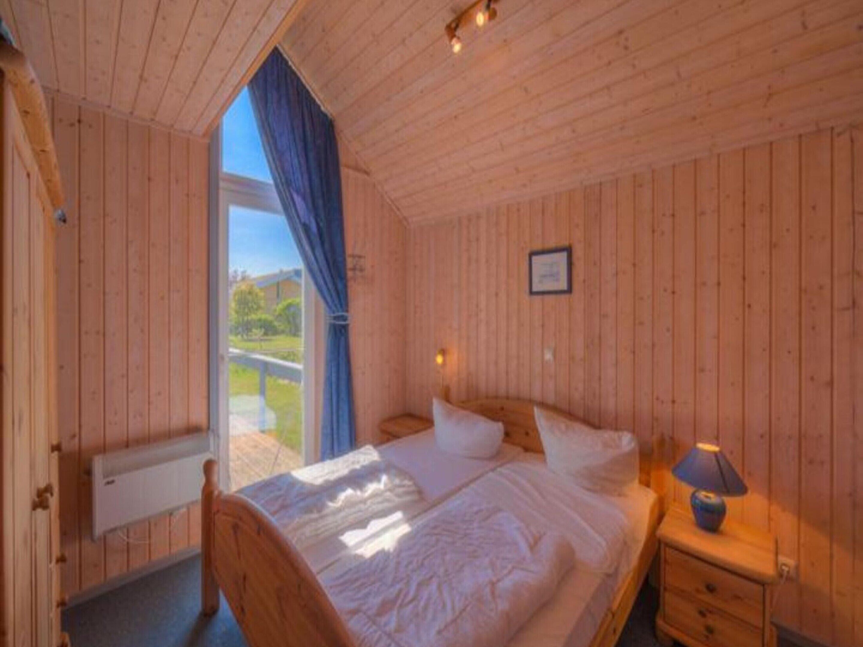 A wooden cabin bedroom with a bed, bedside table, and a window with curtains.