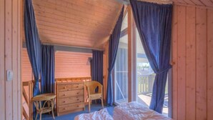 Une chambre à coucher comprenant un lit, une commode, une chaise et donnant sur l’extérieur.