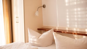A hotel room with a bed, pillows, a nightstand, a lamp, and a window with curtains. - Elegant Eingerichtete Ferienwohnung (Mirow)