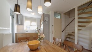 A modern kitchen with wooden cabinets, a large wooden table, and pendant lighting. - Holiday Home in Quiet Park With Garden (Wemeldinge)