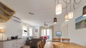 A modern living space with a wooden dining table, a sofa, a TV, and a ceiling fan. - Holiday Home in Quiet Park With Garden (Wemeldinge)