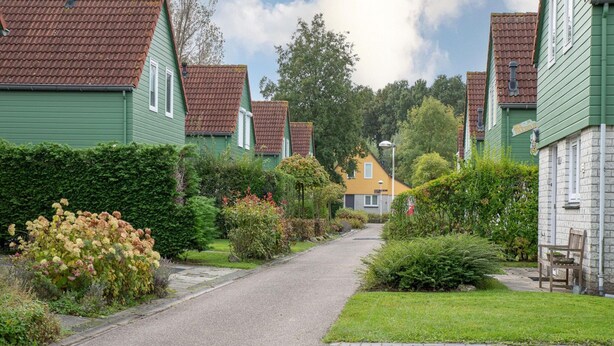 A residential street with houses, a paved path, and greenery. - Holiday Home in Quiet Park With Garden (Wemeldinge)