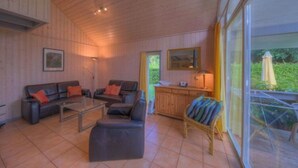 Ett mysigt vardagsrum med en soffa, ett soffbord och en fåtölj i rotting. Det finns också en köksdel med en arbetsbänk och ett fönster.