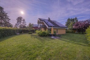Ein Haus mit geneigtem Dach, Solaranlagen, einer Terrasse mit Tisch und Stühlen und einem gepflegten Rasen.
