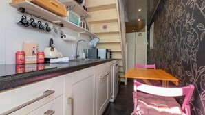 A compact kitchen with white cabinets, a black countertop, and a wooden table with a pink chair. - Studio in Zoutelande Near Stunning Beaches (Zoutelande)