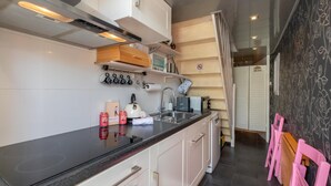 A modern kitchen with white cabinets, a black countertop, and a stainless steel sink. There are hanging kitchen utensils and a small wooden shelf. - Studio in Zoutelande Near Stunning Beaches (Zoutelande)