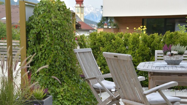 A patio area with two wooden lounge chairs, a round table, and a variety of potted plants. - Chalet in Fulpmes Near Stubai Glacier Skiing (Fulpmes)