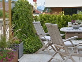 A patio area with two wooden lounge chairs, a round table, and a variety of potted plants.