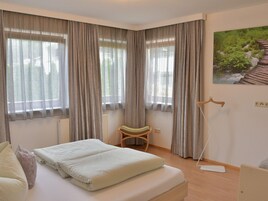 A bedroom with a bed, a chair, a radiator, and a painting on the wall.