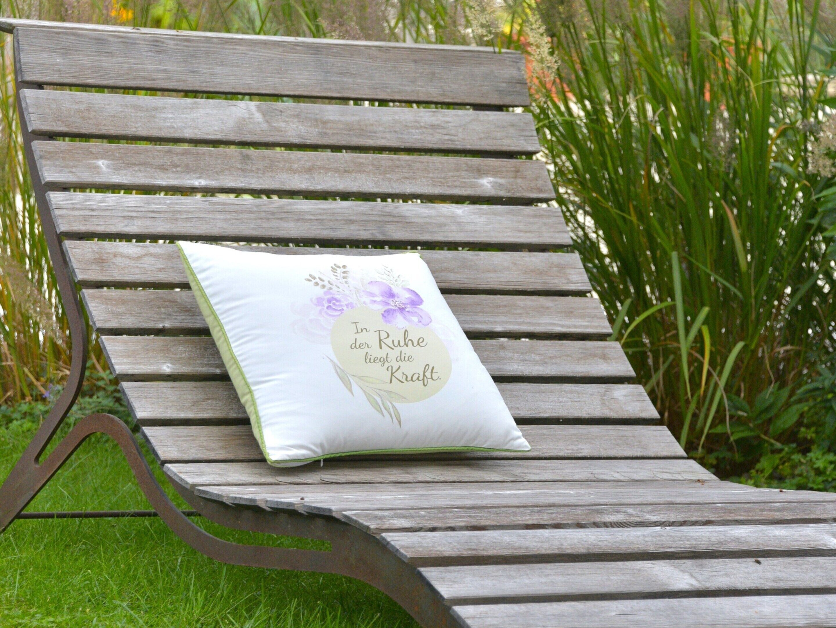 A wooden bench with a cushion featuring floral designs and text.