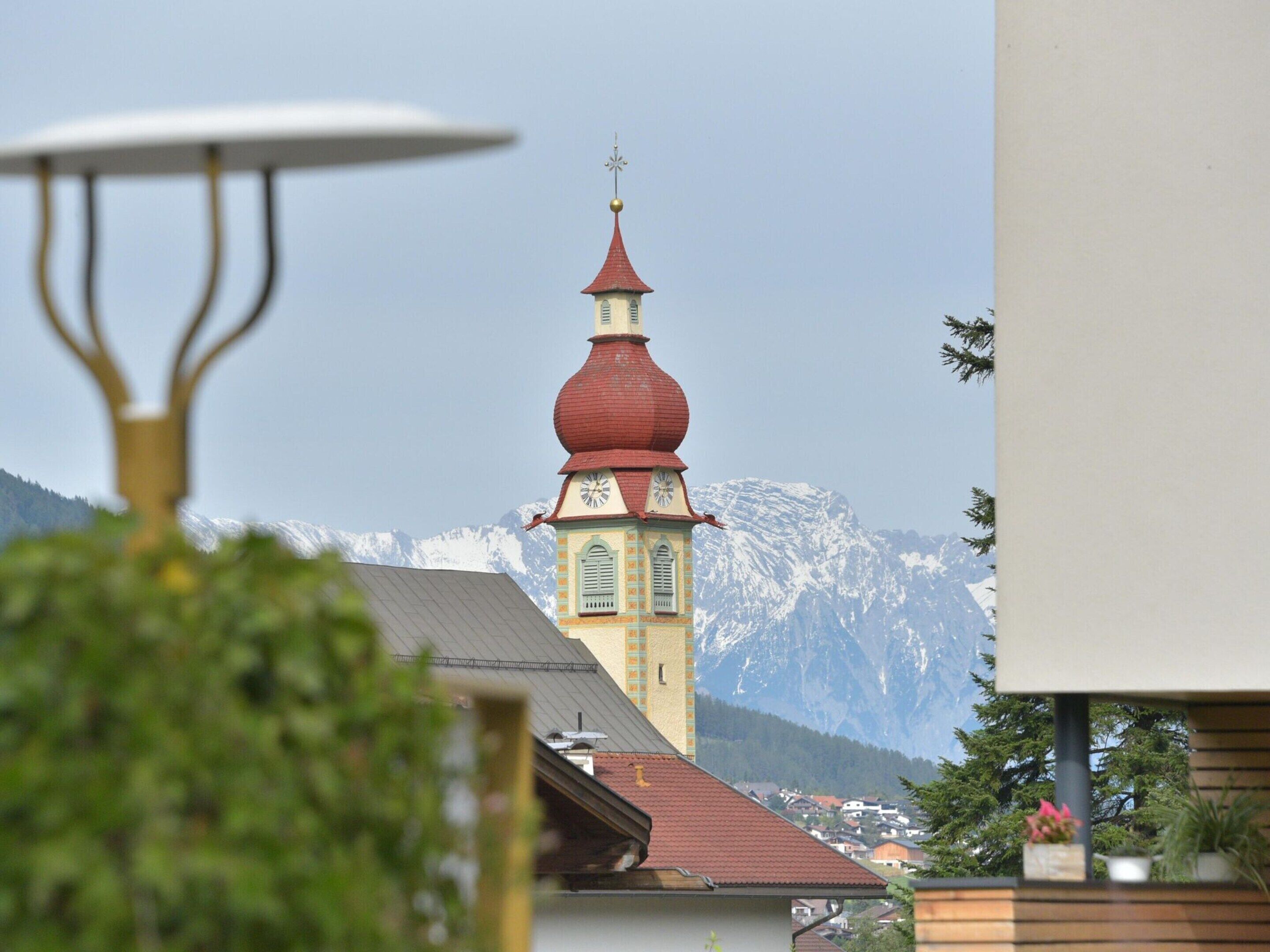 Une église dotée d’un dôme rouge et d’un clocher, entourée de montagnes et d’immeubles d’habitation.