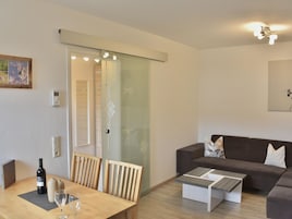 A modern living room with a wooden dining table, a sofa, and a coffee table. There is a sliding glass door leading to another room.