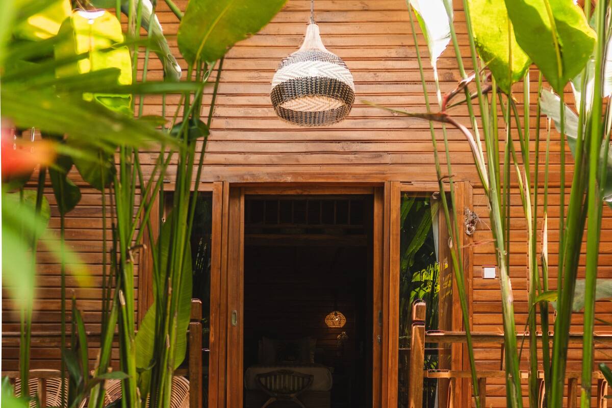 A wooden house with a porch, surrounded by lush greenery.