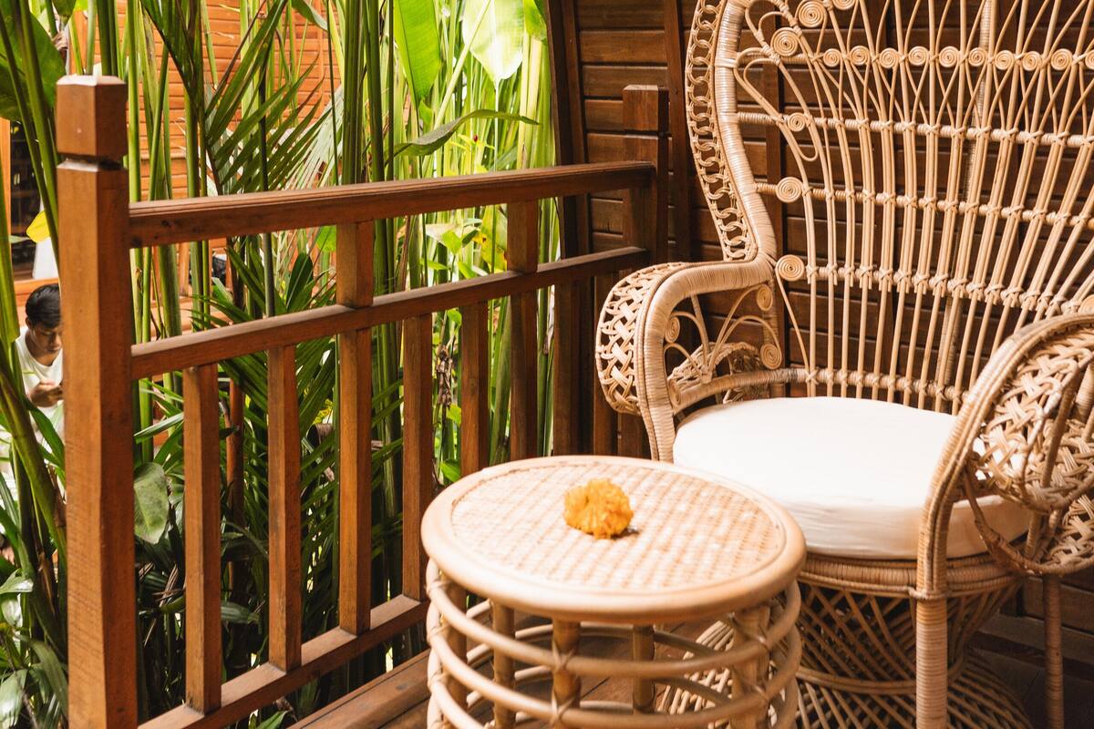 A wicker chair and stool on a wooden deck with a view of lush greenery.