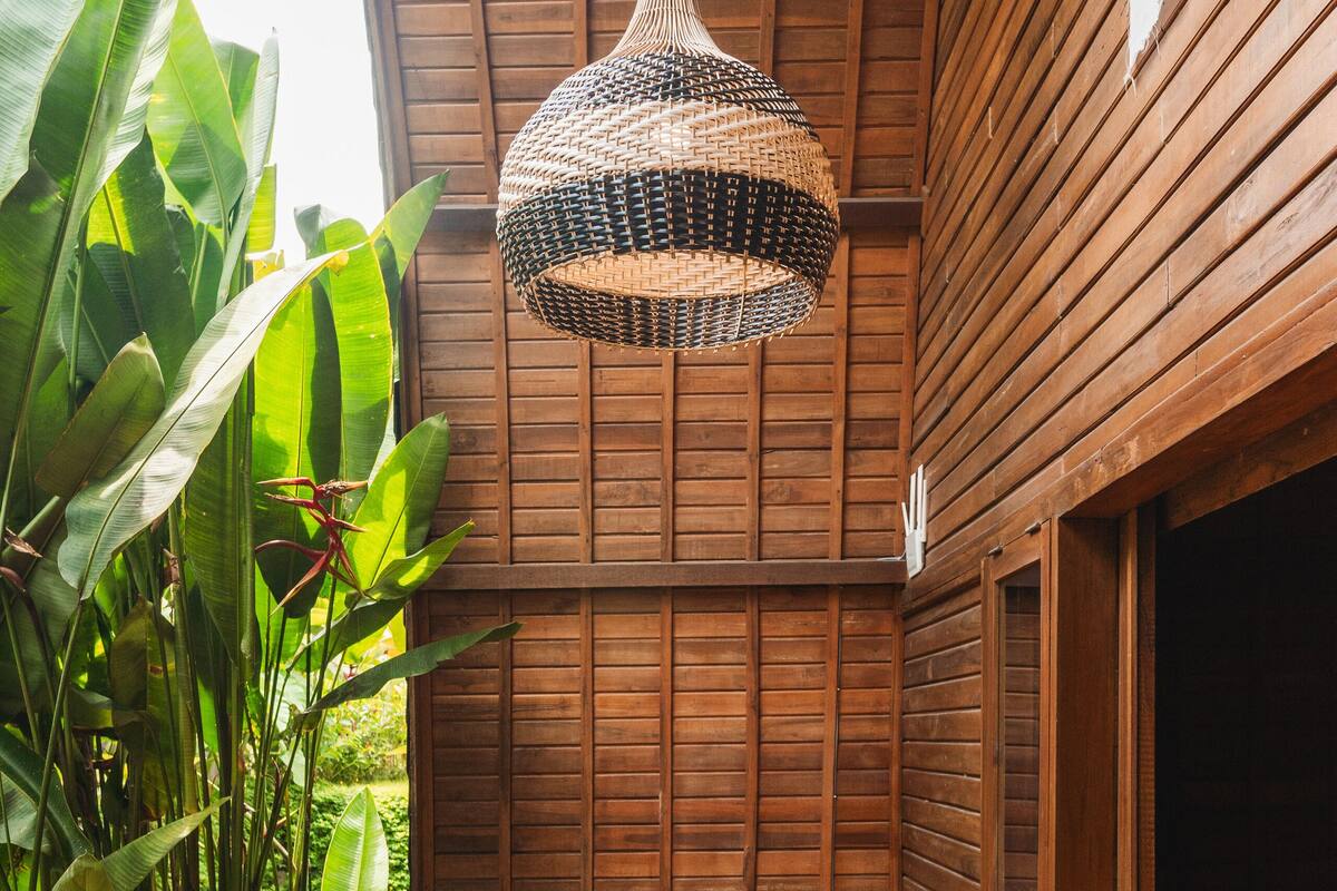 A wooden balcony with a woven pendant light, wicker chairs, and a small round table.