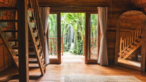 A wooden interior with a staircase leading to a glass door opening to a garden. - Lumeria Yoga (Ubud)