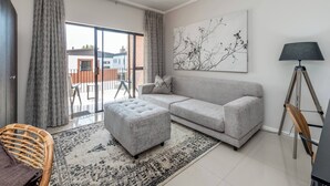 Ein modernes Wohnzimmer mit grauem Sofa, passendem Hocker, einem schwarz-weißen Teppich, einem Holzstuhl und einer Stehlampe.