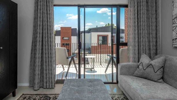 Ein modernes Wohnzimmer mit grauem Sofa, Couchtisch und Balkon mit Glastür.