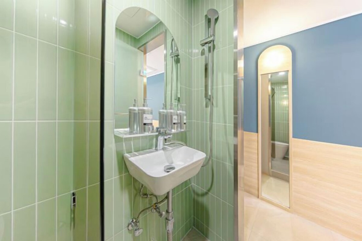 A bathroom with green tiles, a white sink, and a shower.