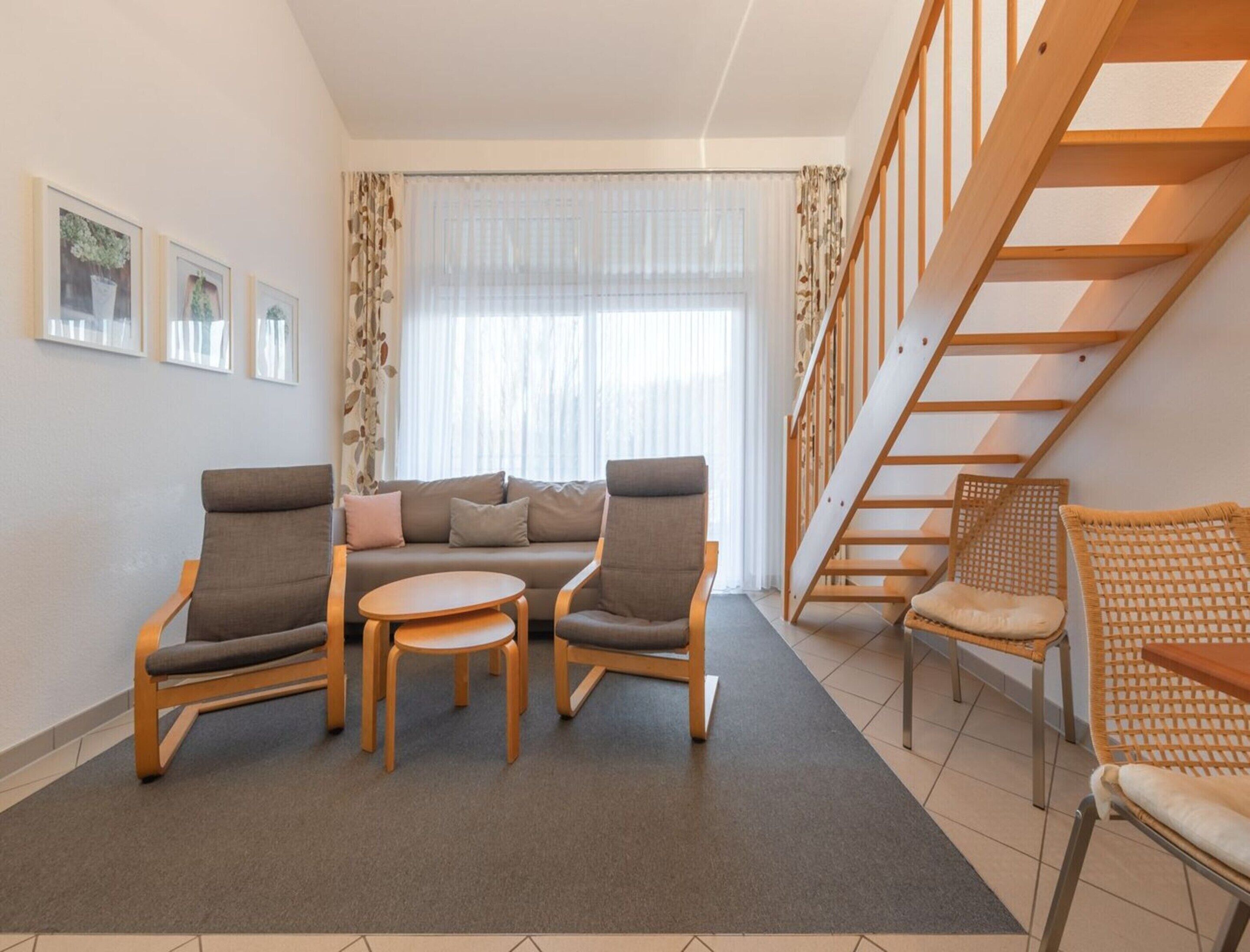 A modern living room with a sofa, two armchairs, a coffee table, and a staircase.